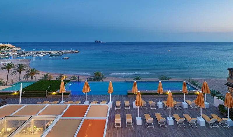 Porto Poniente: Pool terrace, Deck with loungers and orange parasols over the beach