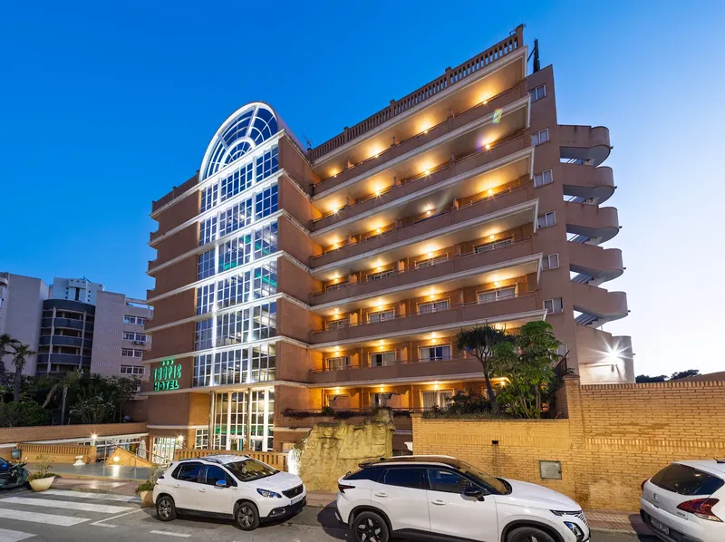 Tropic Relax: The hotel at night, Hotel facade with lit balconies and arched glass tower at dusk