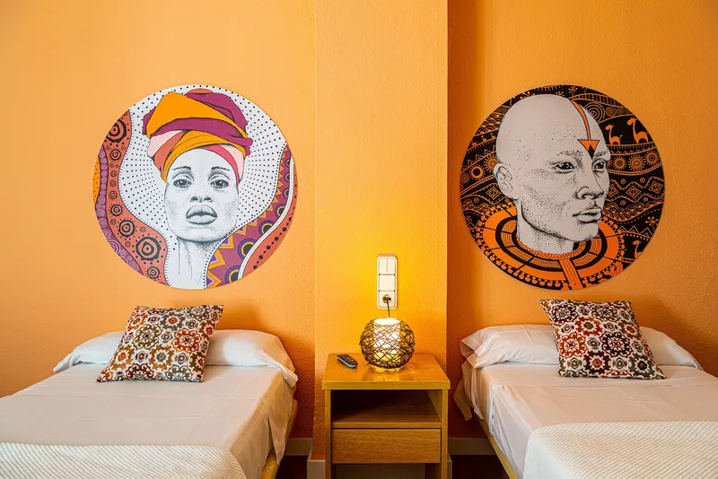 Internacional: Twin room, Twin beds against an orange wall with portrait artwork