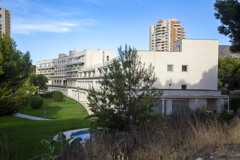 Benidorm Poniente: The hotel, Low white building above green gardens