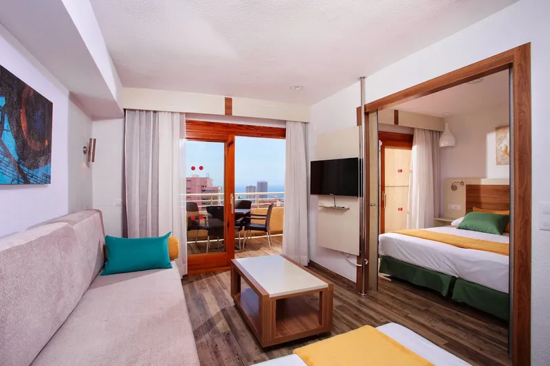 Sandos Suites: Suite lounge, Sofa and TV with bedroom and balcony beyond