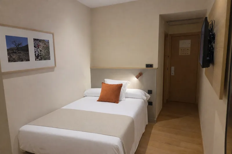 Tanit: Single room, Single bed with orange cushion and wall TV
