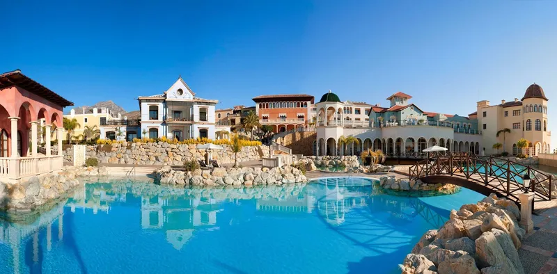 The Level: Pool and village, Pool and footbridge in front of colourful village-style buildings